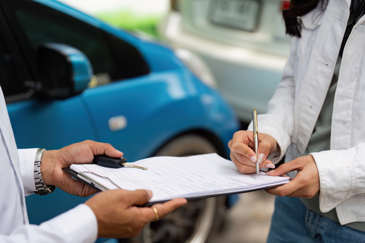 A woman signing car insurance paperwork while discussing details with an agent