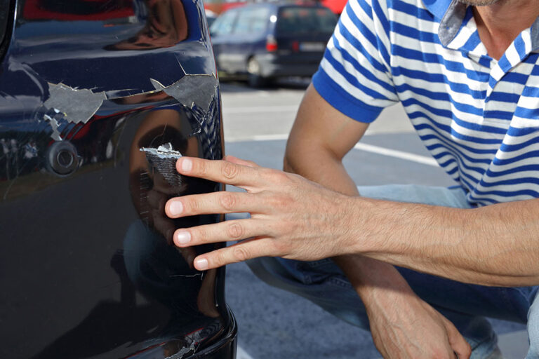 Car damaged in parking lot. Man checking car scratches and dents
